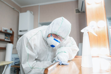 Coronavirus Pandemic. A disinfector in a protective suit and mask sprays disinfectants in house or...