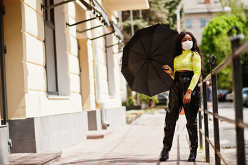 African American woman posing with facial mask to protect from infections from bacteria, viruses and epidemics and hold umbrella.