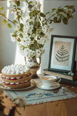 Raspberry vanilla cake on a wooden backdrop with bouquet of pear flowers and sunlight
