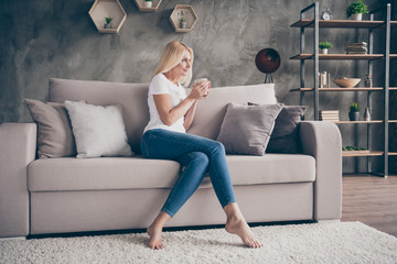 Portrait of her she nice attractive lovable pretty charming dreamy mature lady sitting on divan resting relaxing drinking beverage in modern industrial loft interior style apartment house