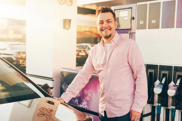 A young smiling european man refueling his car with petrol at the gas station