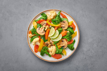 Pad Pak Ruam or Veg Thai Stir-Fried Vegetables in white plate on gray concrete backdrop. Pad Pak is thailand cuisine vegetarian dish with mix of vegetables and sauces. Thai Food. Copy space. Top view