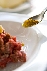 Adding cumin to the heap of ground meet in white plate for cooking