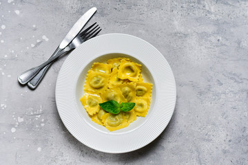 Ravioli with ricotta and spinach in a white plate on a grey stone table. Recipe of Italian pasta, gourmet lunch.  Top view , copy space , food  flat lay