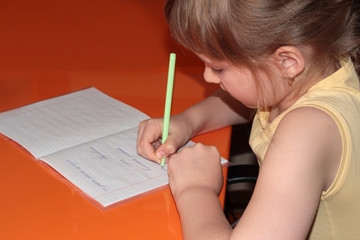 A girl does her homework on an orange table. A child in a yellow coverlet writes in a notebook.