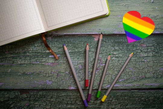 Heart painted rainbow, colorful pencils and notebook on wooden green background. LGBTQ concept. Flat lay