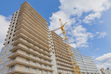 A house of concrete and metal and a construction crane, modern technology, a skyscraper against a blue sky.