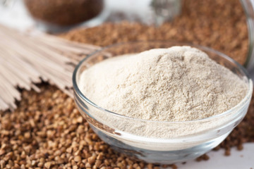 buckwheat is scattered on a table made of a glass jar, next to it is a plate with buckwheat flour and lies soba