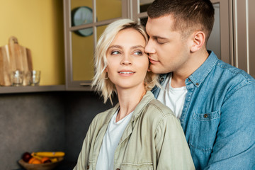 smiling young loving couple hugging in kitchen at home