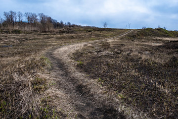 A winding narrow path on the ground with last year’s dry grass climbing a hill.