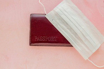 Passport in a brown cover and medical mask on a pink background