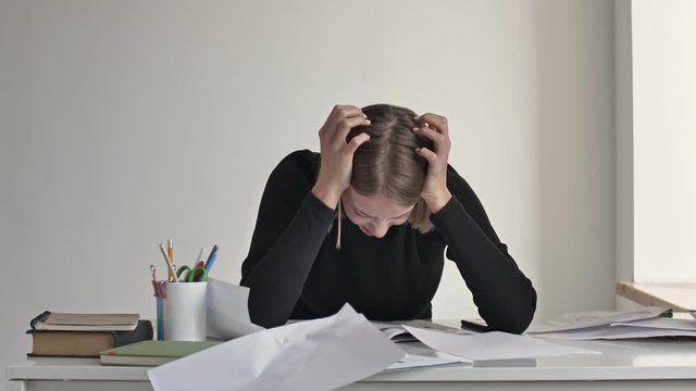 A serious tired young blonde businesswoman is throwing up paper documents while working indoors in a white office is throws up