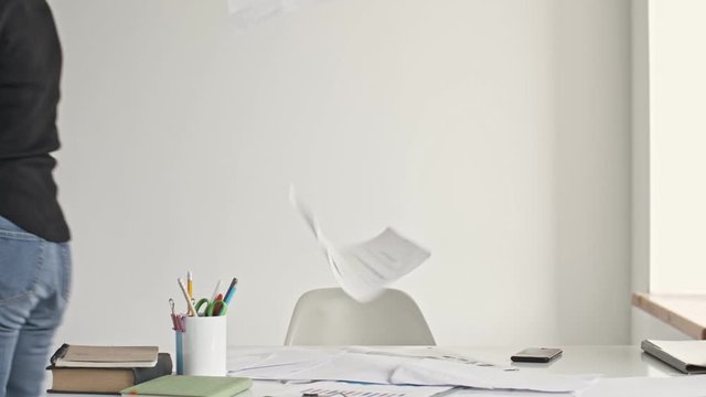 A displeased tired young blonde businesswoman is throwing up paper documents and goes away in a white office is throws up