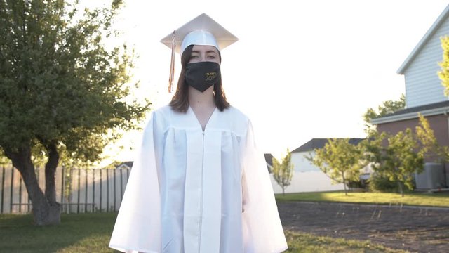 2020 graduate walking forward wearing face mask with cap and gown.