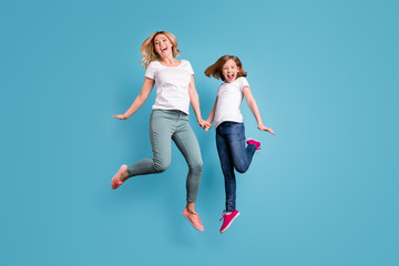 Fototapeta na wymiar Full length photo of funny mom lady little daughter spend time together jumping high up hold hands good mood wear casual white s-shirts isolated blue color background
