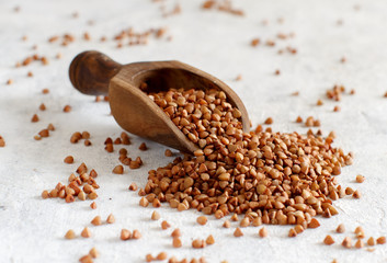 Raw dry buckwheat grain with a spoon on a white table
