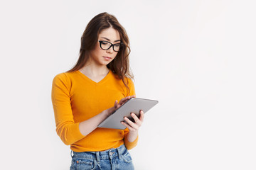 A beautiful young girl in glasses with a tablet in her hands poses on a light background. Education, distance learning. Space for text