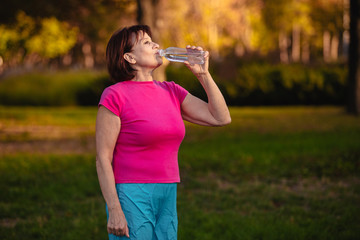 Elderly woman Drinking water from a bottle at sunset