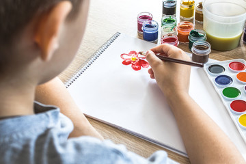 The child draws gouache on a white sheet and jars of paint are on the table. Hobbies and entertainment for children.