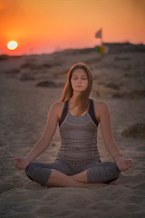 Fototapeta na wymiar Young blond woman is meditating on a seaside in Healthy Pose on Beach in Sun Light Rays, Yoga Meditation practice concept