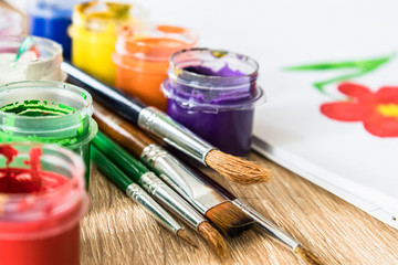 On the table are multi-colored gouache in a jar and brushes for painting. Set for drawing, creativity and hobbies.