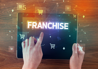 Close-up of a hand holding tablet with FRANCHISE inscription, online shopping concept