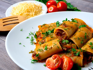 stuffed pasta paccheri with minced meat with tomato sauce and herbs on a white plate