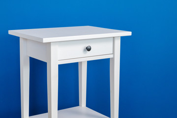 White wooden nightstand table against blue wall, modern furniture