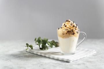 Dalgona frothy coffee in a transparent glass cup decorated with chocolate drops, trend korean drink made with milk and coffee foam on grey background