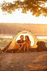 A man and a woman are sitting in a tent at sunset. Honeymoon in the hike