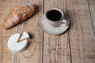 
Camembert cheese with white mold, coffee and croissant. Tasty gourmet breakfast on wooden background.