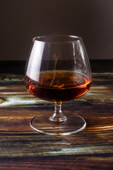 
Glass with cognac on a brown wooden background. Strong expensive alcoholic drink.