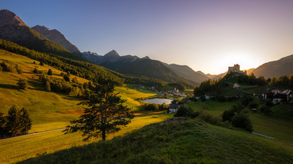 Fototapeta premium Sun is setting at the mountains surrounding Tarasp and its castle, in the canton of Graubünden (Engadin) Switzerland. The castle is a Swiss heritage site of national significance
