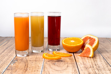 Three different fruit juices in glasses and fruits on a wooden background. Healthy nutrition for children and adults. Orange, cherry and tropical juice.