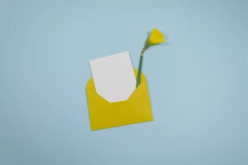 Foto op Canvas Minimalistic composition with a beautiful festive yellow mustard envelope, white blank card and Narcis flower on a trendy blue pastel background. Place for text. Flat lay. Top view © Anna