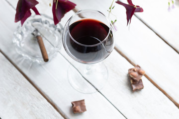 red wine in a glass on white wooden table with chocolate, cigar, plant leaves