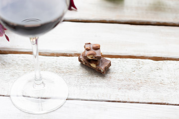 dark chocolate pieces with nuts on white wooden background and red wine glass