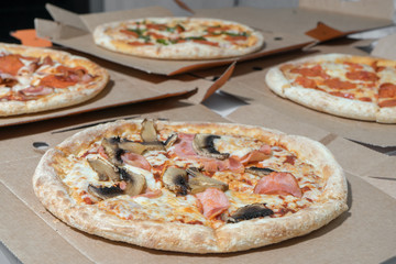 Close up of pizzas with variety of toppings, mushrooms and cheese in cardboard boxes with open lids