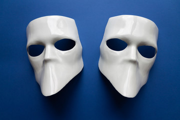 Theatre concept with the white masks on classic blue background. Anonimous, Incognito, Conspiracy concept. Place for text. Flat lay style. Top view