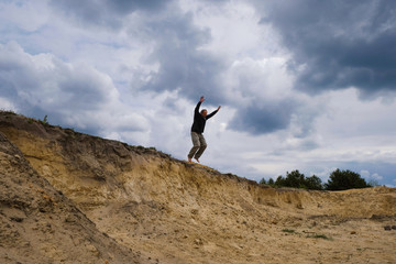 Sand quarry and silhouette of a sporty man jumping down on a background of rain clouds. Ukraine. Freedom concept.