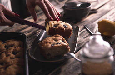 Close up of female chefs hands servicing slice of cake with cherries on dark background.
