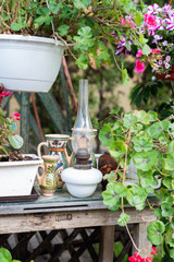 Vintage oil lamp and folk art jugs in the garden - pots of flowers on a table