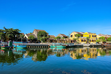 Fototapeta na wymiar Hoi An ancient town in the sunshine day with blue sky, fishing boats, ancient houses reflect on the river. Hoi An is a popular tourist destination in Quang Nam, Vietnam. Landscape photography.