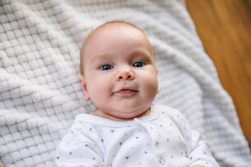 Newborn baby two-months-old smiles and lies on a white blanket. Psychomotor development and baby care