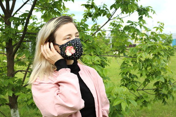 Woman wearing cloth cotton face mask decorated with flowers at the street. Stylish handmade cotton designed face mask. 