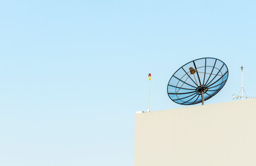 Satellite dish antenna mounted on rooftop in urban area on clear blue sky