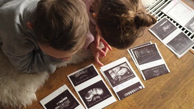 children lying on floor and  watching pregnancy ultrasound prints