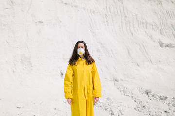 Young woman walking on a phosphate mountain that was made by chemical plant waste. She is wearing yellow protective coat and a mask. Ecology protection awareness