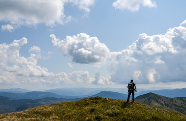 Hiker with backpack standing on a top of a mountain enjoying lookout view of mountains. Nature landscape in Carpathians. Healthy active lifestyle.
