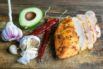 Spicy baked chicken breast with peper, rosemary, avocado and garlic on wooden cutting board on...